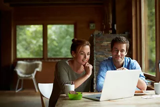 Smiling young couple using laptop while having coffee at table in cottage